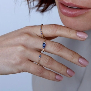 Detailed view of layered 18K gold plated rings with emerald-cut blue sapphire and diamonds
