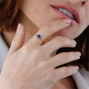 Macro detail of gold plated silver ring with blue emerald cut stone on finger