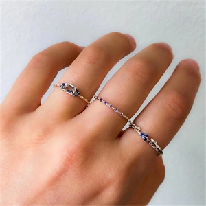 Close-up of stacked thin gold rings featuring blue, purple gemstones and twisted vine details