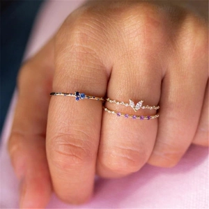 Close-up of three layered gold rings with blue, purple, and white zircon gemstones on hand