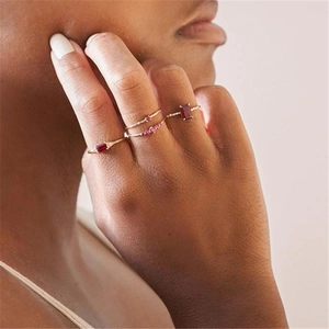Detail of four thin gold rings with red gems and sparkling stones on female hand