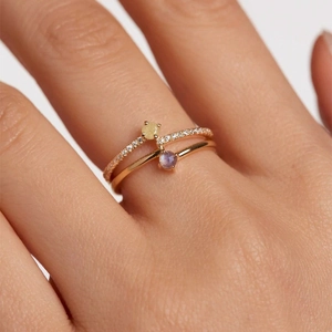 Detail of a double-layered gold ring with yellow and purple gemstones worn on a finger