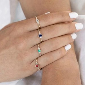 Detailed view of four stacked minimalist gold rings with colorful gemstones on a finger