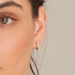 Macro view of gold hoop earring with square-cut cubic zirconia on a model's ear