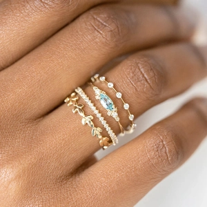 Macro shot of stacked gold rings featuring marquise blue gemstone and leafy accents