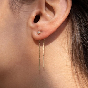 Dettaglio di orecchini a catenella dorati con piccola pietra di zircone su una modella