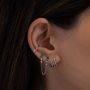 Detail of silver drop earrings with green gemstones and a snake-shaped diamond ear cuff