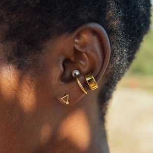 Macro shot of gold ear cuff set with pearl and dainty diamond chain on model's ear