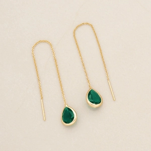 Dettaglio ravvicinato di orecchini a goccia color smeraldo con catenine in argento dorato