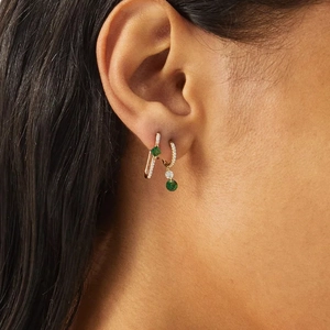 Detalle de pendientes imperdibles dorados con piedras esmeralda y micropavé de diamantes