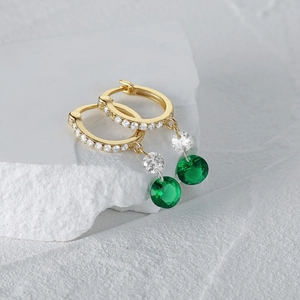Vista macro de pendientes de aro dorados con esmeralda verde brillante y circonitas blancas