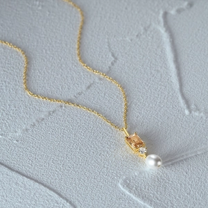 Dettaglio ravvicinato di una collana d'oro con gemma ambra e ciondolo di perla su pietra