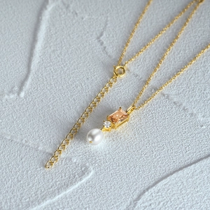 Dettaglio macro della collana d'oro con gemma arancione, zircone e perla bianca