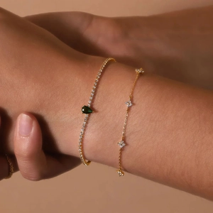 Detail of 18K gold plated tennis bracelet featuring teardrop emerald stone and floral chain