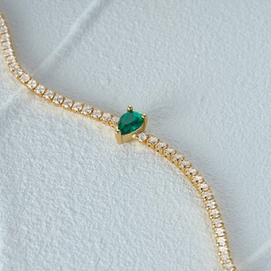 Macro shot of gold tennis bracelet with a green pear-cut stone and sparkling crystals