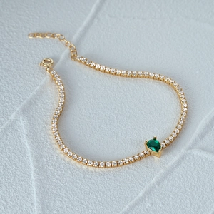 Detail of gold tennis bracelet with white CZ and a pear-cut emerald green gemstone
