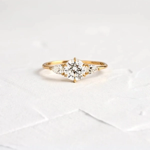 Dettaglio macro di anello in oro con diamante tondo centrale e pietre laterali a pera