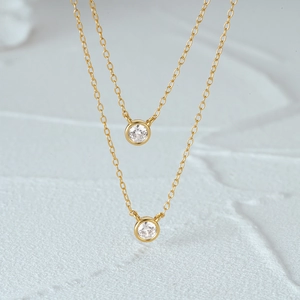Detail of two layered gold S925 silver necklaces with round bezel-set solitaire diamonds