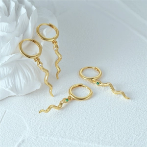 Nahaufnahme von goldenen Schlangenohrringen mit weißen Kristallen und grünen Augen