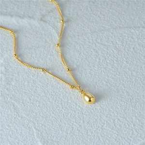 Makro-Detail einer goldenen Tropfen-Halskette mit filigraner Perlenkette und Metallglanz