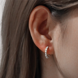 Detail of silver S925 huggie earring with white cubic zirconia worn on an ear