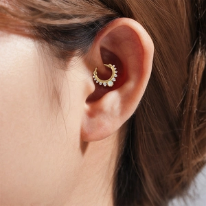 Close-up of gold daith piercing ring with white opal and sparkling cubic zirconia