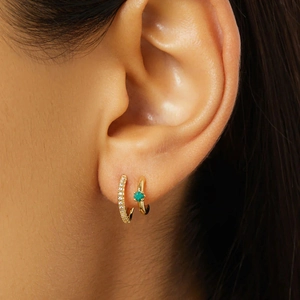 Primer plano de aretes huggie dorados con pavé de gemas y una esmeralda cuadrada única
