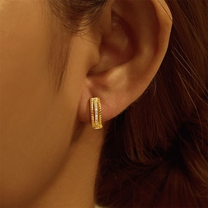 Detail of gold huggie earrings with twisted rope texture and sparkling zircons on ear
