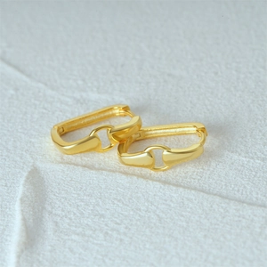Macro shot of gold horsebit earrings with a polished finish on textured background