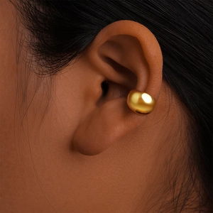 Dettaglio ravvicinato di un ear cuff a forma di C dorato opaco indossato sull'orecchio