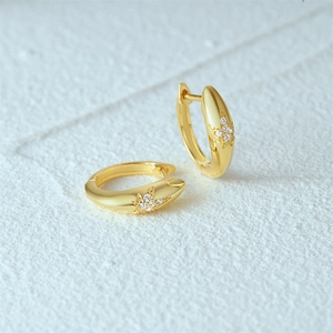 Close-up of gold hoop earrings with star leaf zircon pattern on white fabric