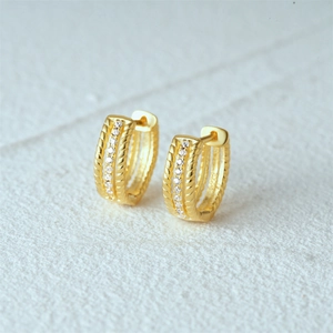 Macro shot of gold U-shaped hoop earrings with twisted rope texture and CZ inlay