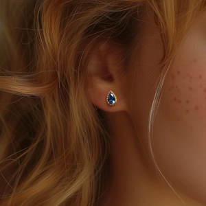 Detailopname van blauwe druppelvormige zirkoon oorbel met gouden kraalrand
