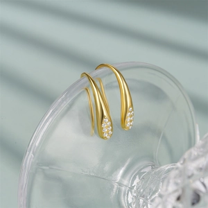Macro shot of gold waterdrop earrings with zircon inlay hanging on a glass rim