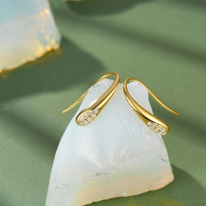 Close-up of gold water drop earrings with sparkling pavé zircons on white stone
