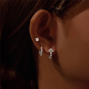 Primo piano di orecchini in argento 925 con croci di zirconi colorati indossati sul lobo