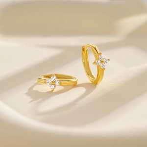 Close-up of gold hoop earrings with sparkling zircon four-petal flower charms