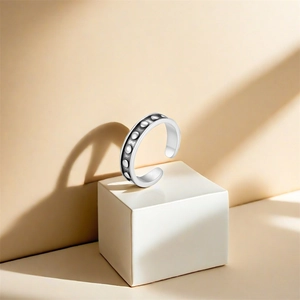 Macro detail of silver lotus toe ring featuring oxidized vintage studs on a white cube