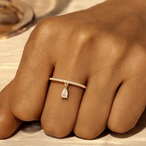 Close-up of a gold s925 silver ring featuring pavé zircons and a pear-shaped drop pendant