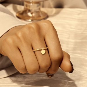 Minimalist gold thin ring with heart pendant shown on finger against silk fabric