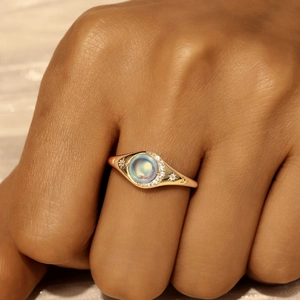 Detail of 18K gold ring with round moonstone and star engravings on a model's hand