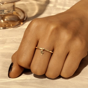 Detail of a minimalist gold ring with a small cross charm worn on the finger