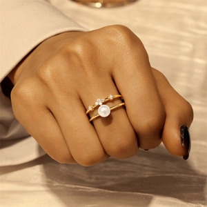 Close-up of gold layered rings with white pearl and sparkling zircon on silk fabric