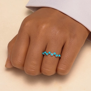 Detail view of wavy silver band set with turquoise stones on a person's finger
