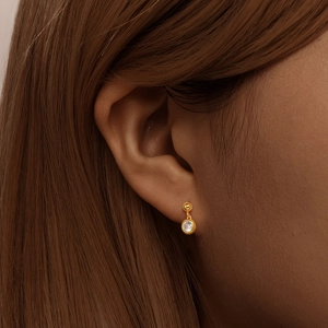 Close-up of S925 silver 18K gold earrings featuring a round white zircon on the ear lobe