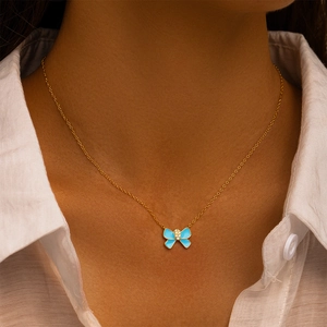 Close-up van een gouden vlinderketting met blauw email en diamanten op een model
