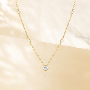 Detail of gold bezel-set station necklace with five sparkling round diamonds on a fine chain