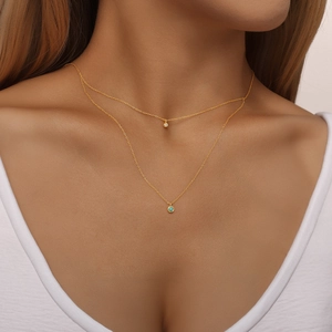 Detail einer zweilagigen Goldkette mit Kristall- und Türkis-Anhänger an einem Model getragen
