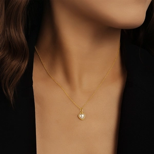 Gros plan d'un pendentif cœur en perle sur une chaîne dorée portée par un mannequin