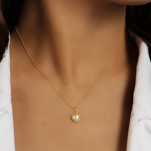 Gros plan d'un pendentif en perle en forme de cœur sur un collier doré porté